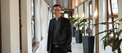 Weihbischof Martin Marahrens steht in einem Flur und lächelt in die Kamera, eine Hand in der Hosentasche