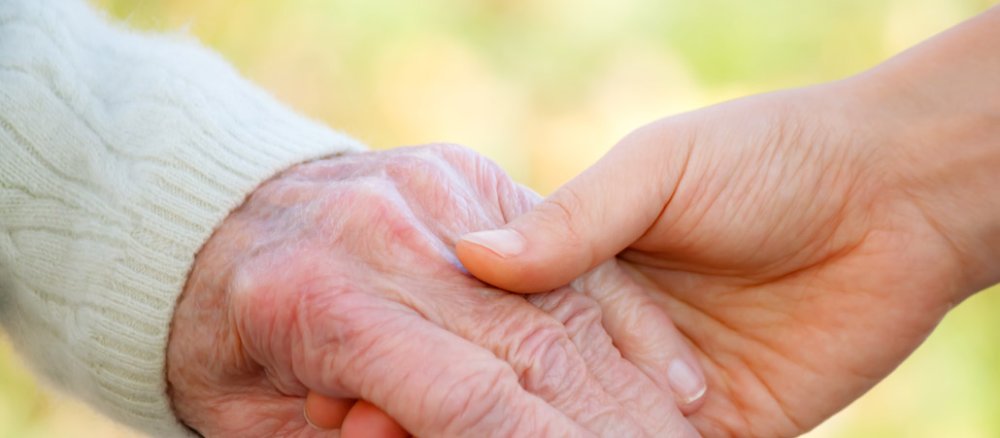 Ein alter ein junger Mensch geben sich die Hand.