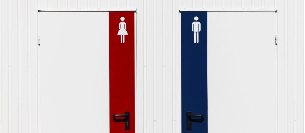 Zwei Toilettentüren, eine mit rotem Streifen und Frau-Symbol, eine mit blauem Streifen und Mann-Symbol.
