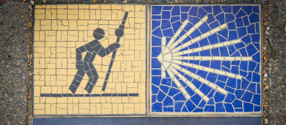 Signpost on a house wall with the pictogram of a pilgrim and a yellow shell for the Way of St James