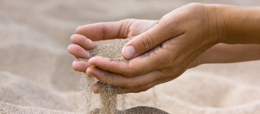 Sand läuft zwischen den Fingern einer Frau hindurch