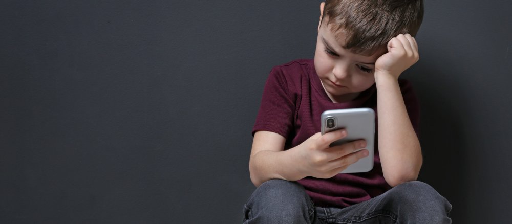 Ein Kind schaut traurig auf sein Smartphone.