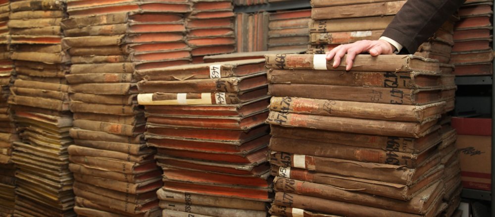Eine Hand stützt sich auf einen Stapel Kirchenbücher im Archiv