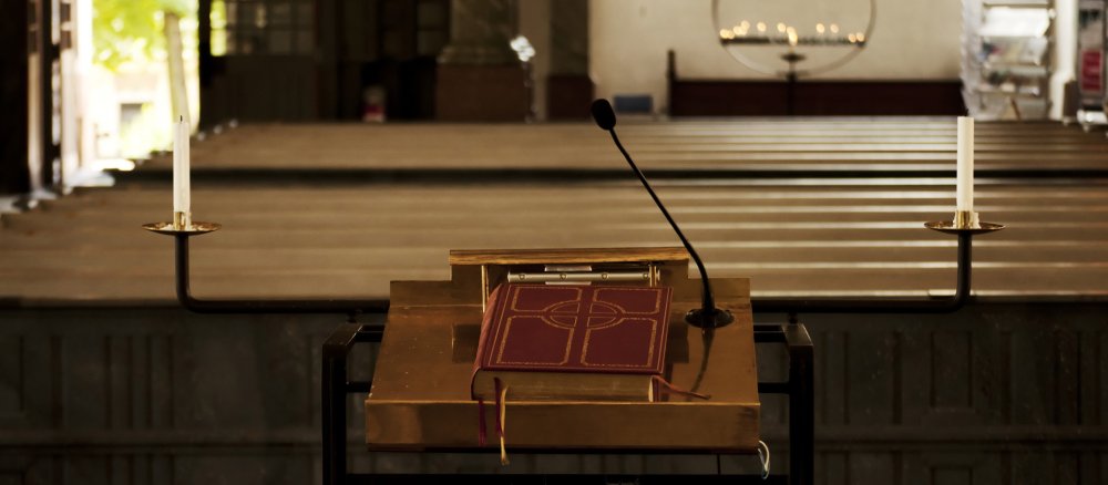 Eine Bibel liegt auf dem Ambo vor leeren Kirchenbänken.