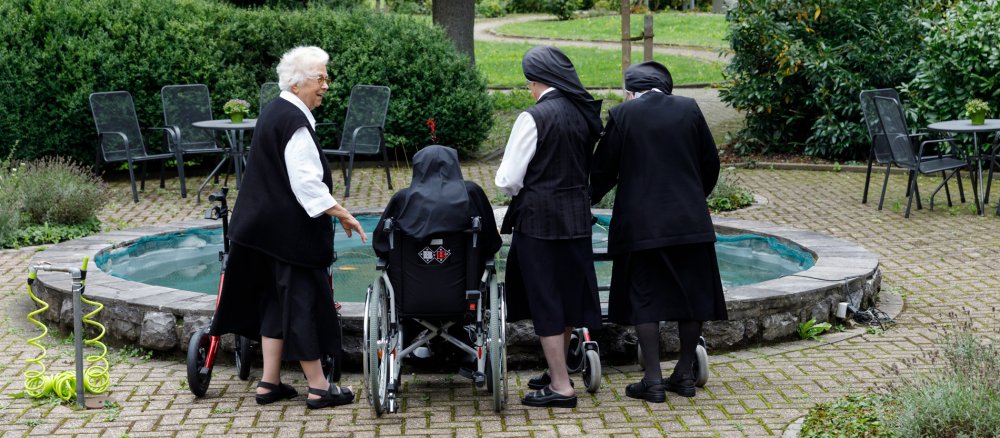 Vier Ordensfrauen stehen um einen kleinen Teich im Klostergarten.
