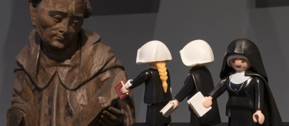 Playmobil-Figuren vor einer historischen Mönchsstatue