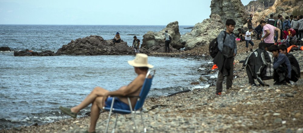 Ein Tourist sitzt am Strand, an dem Flüchtlinge ankommen.