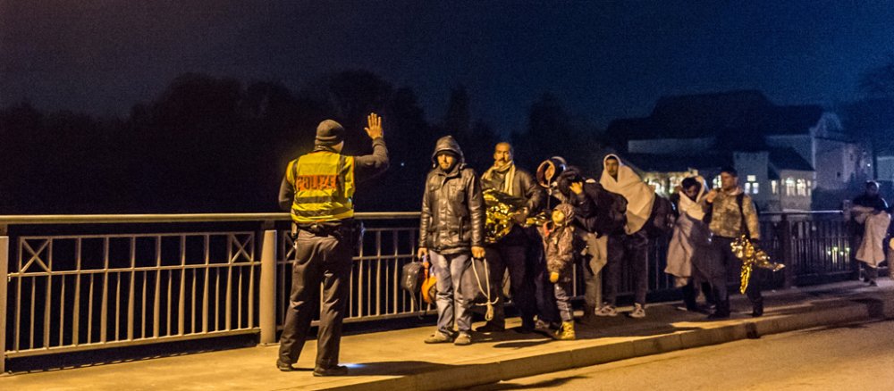 Ein Polizist sammelt an der Deutsch-Österreichischen Grenze eine Gruppe von Geflüchteten auf.