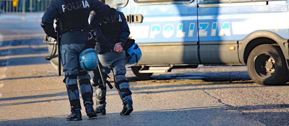 Italienische Polizisten vor einem Polizeiauto.