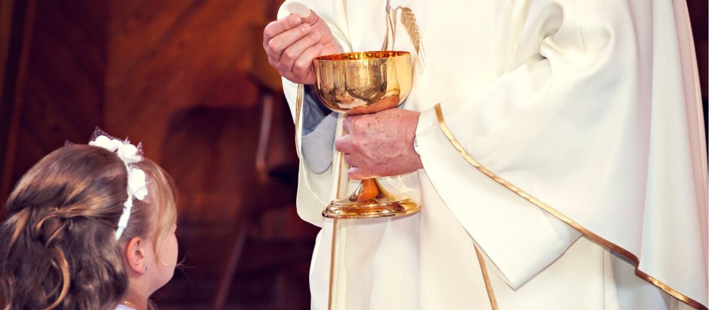 Priester überreicht einem Mädchen die Hostie während der Erstkommunion in einer Kirche.