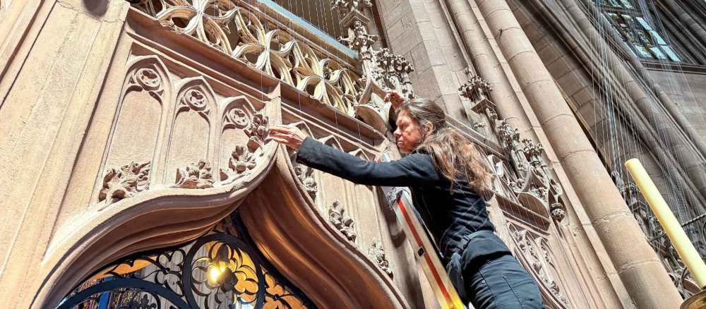 Die Künstlerin steht auf einer Leiter und berührt die dünnen Fäden, die in der Kirche hängen.
