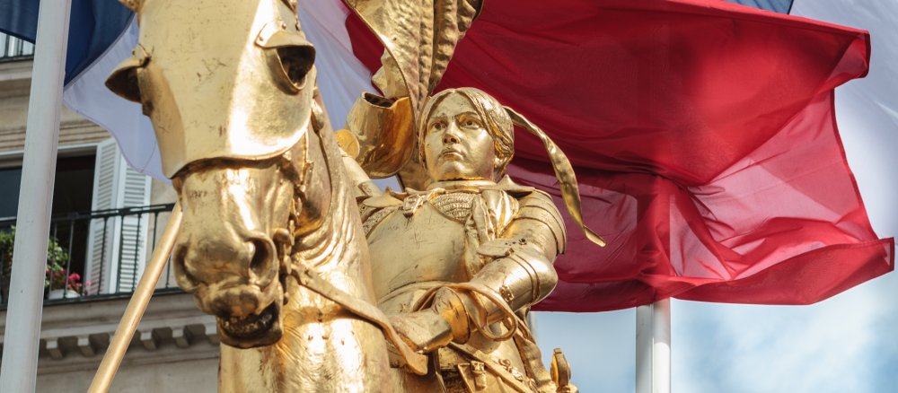 Die goldene Statue von Jeanne d'Arc auf der Place des Pyramides in Paris vor französischen Fahnen.