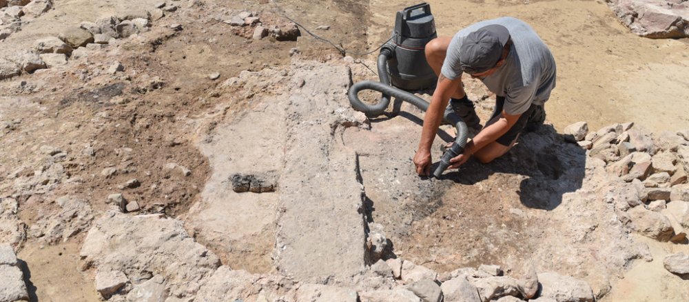 A man cleans the remains of an old baptismal font at an excavation site.