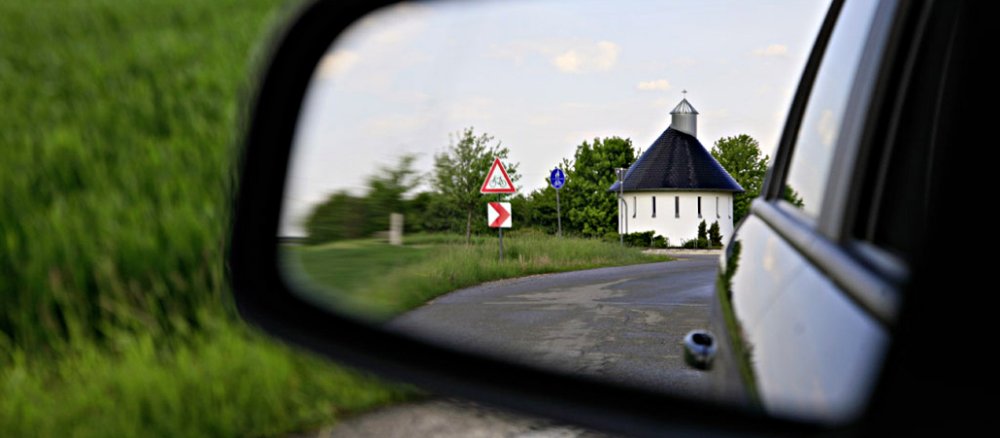 Der Rückspeigel eines Autos zeigt eine weiße Kirche am Straßenrand .