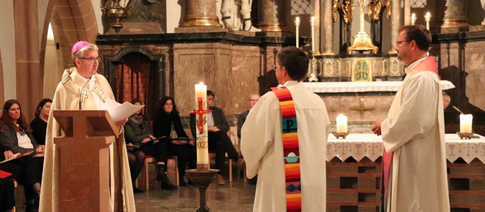 Bischof Peter Kohlgraf überreicht die Dekrete ihrer offiziellen Ernennung zu Beauftragten der queersensiblen Pastoral an Christine Schardt und Matthias Berger.