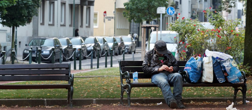 Neben dem Mann stehen vier Tüten mit seinen Habseligkeiten.