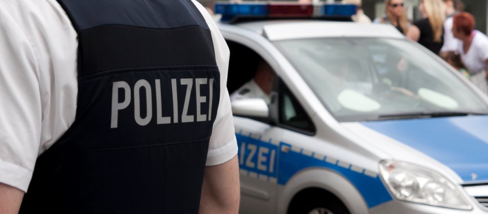 Ein Polizist steht vor seinem Streifenwagen.