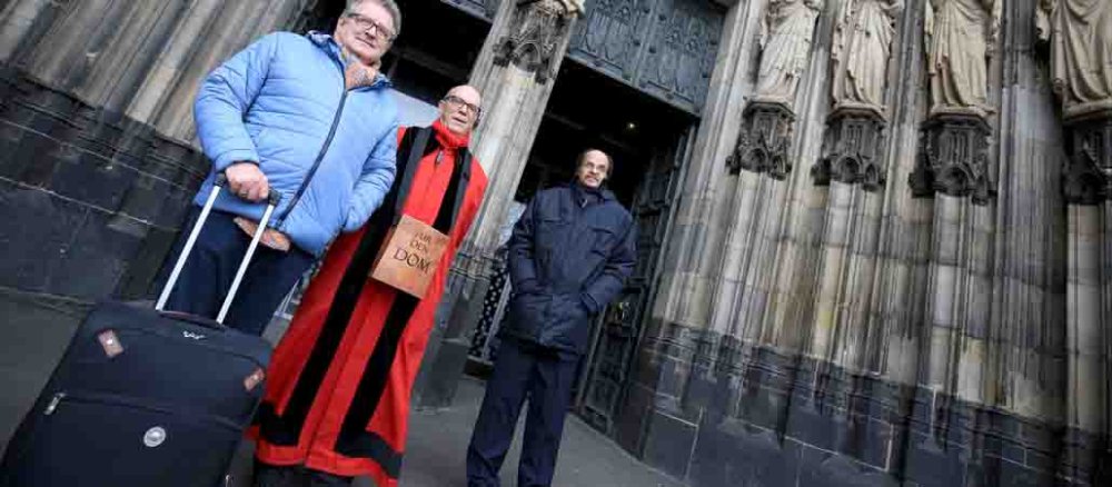 Ein Domschweizer kontrolliert am Kölner Dom einen Mann mit einem Koffer.