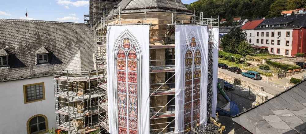Auf großen Planen hängen die Fenster-Entwürfe von Gerhard Richter außen an der Abteikirche von Tholey.