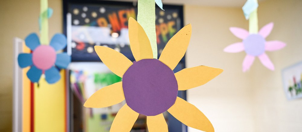 Aus Pappe gebastelte Blumen hängen von der Decke in einer katholischen Kita.
