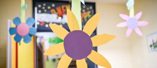 Aus Pappe gebastelte Blumen hängen von der Decke in einer katholischen Kita.