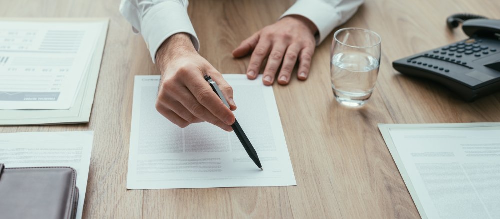 Eine Hand deutet auf ein Papier, das unterschrieben werden soll.