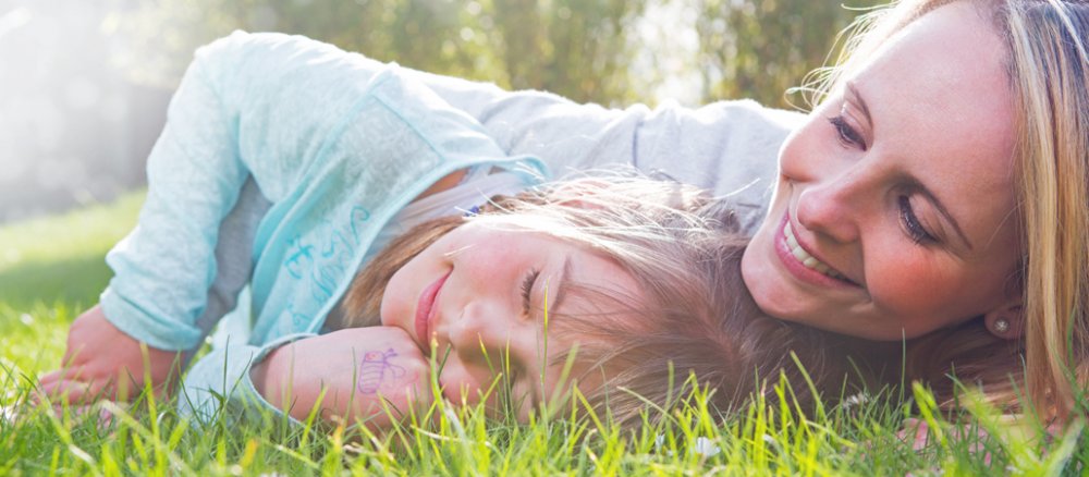 Eine Mutter liegt mit ihrer Tochter im Gras.
