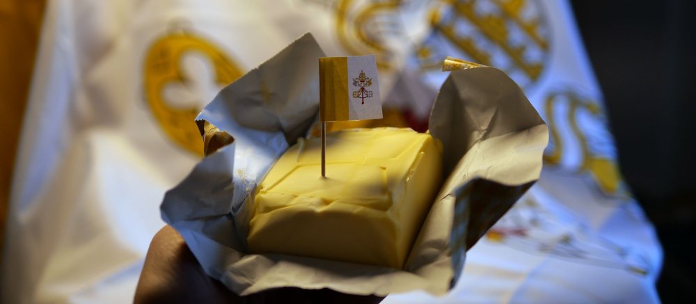 Ein Stück Butter mit Vatikanflagge vor dem Wappen des Vatikans