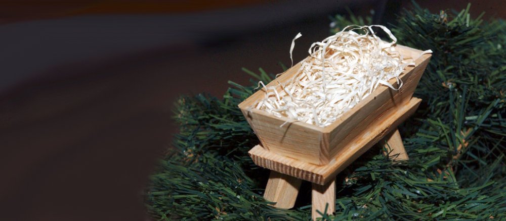 Leere Holzkrippe mit Stroh auf Tannenzweigen