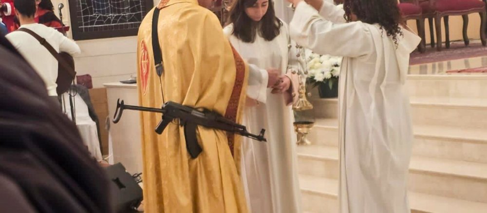 Ein maronitischer Priester trägt ein Maschinengewehr bei der Messe