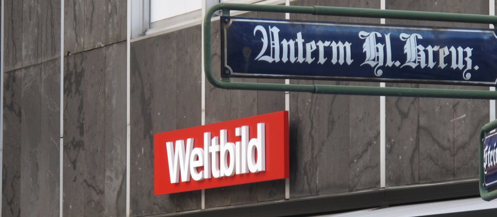 Das Straßenschild "Unterm Heiligen Kreuz" hängt direkt über einem Schild von einer Weltbild-Filiale.
