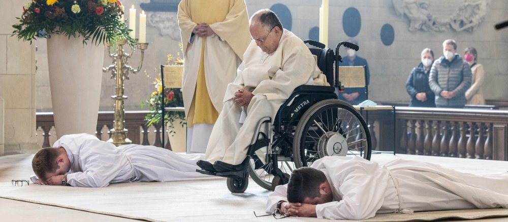 Zwei Männer liegen vor dem Altar, ein Mann im Rollstuhl verbeugt sich.