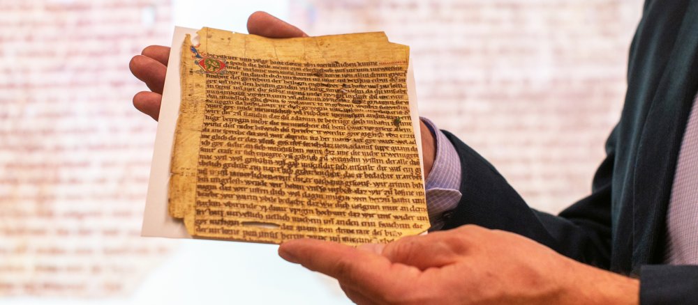 Zwei Hände halten ein Pergamentfragment