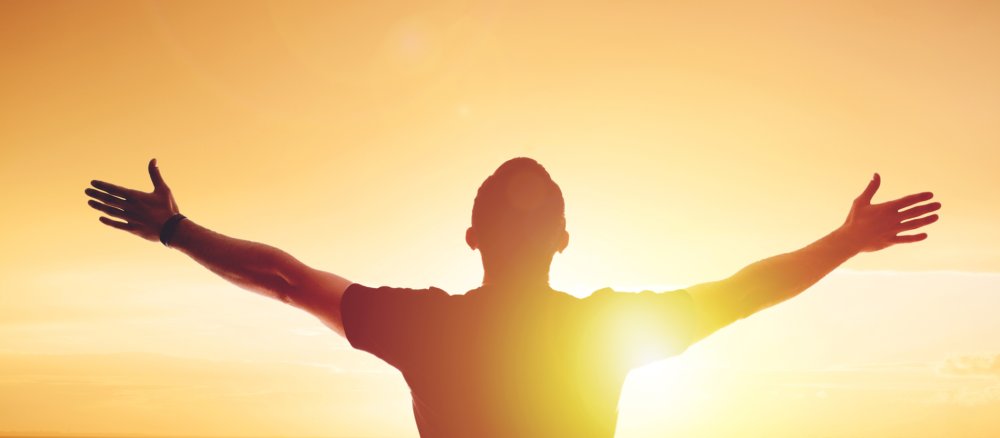 Ein Mann schaut mit ausgebreiteten Armen Richtung Sonnenuntergang