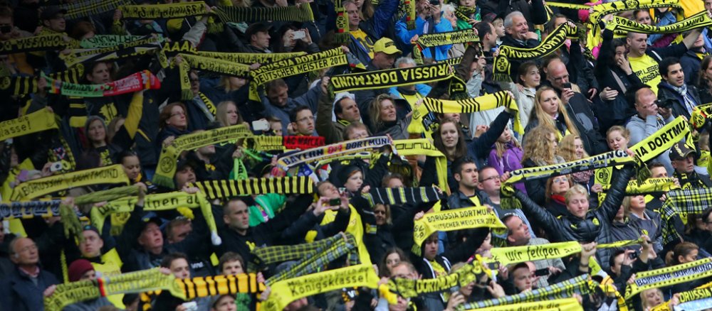 Fans im Stadion auf der Tribüne halten Schals in die Höhe