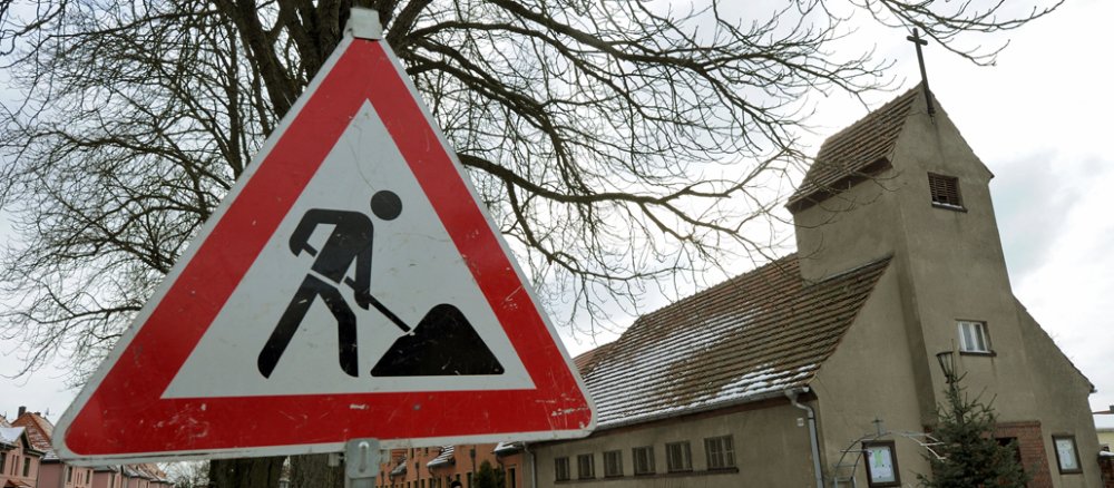 Auf dem Dach der Kirche liegt ein wenig Schnee, davor steht in Baustellenschild.