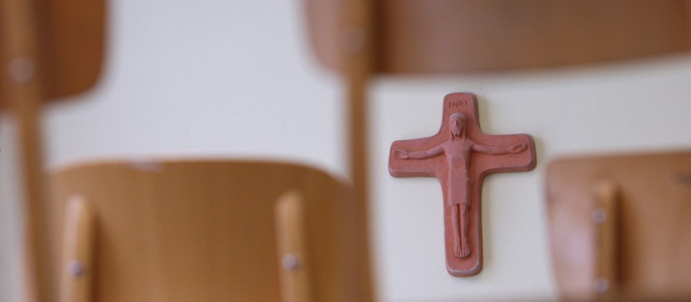 In einem Klassenzimmer hängt ein Kreuz an der Wand.