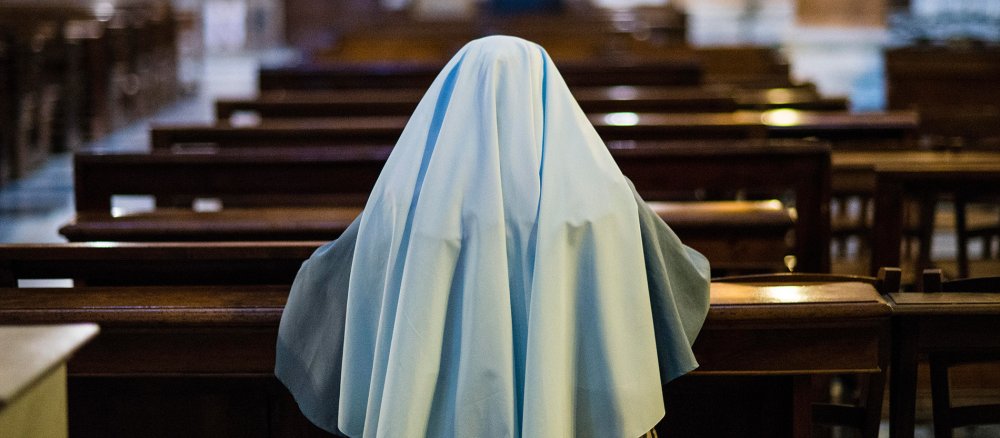A nun prays kneeling in a church pew, back view