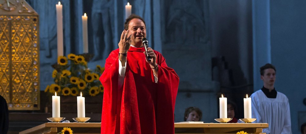 Pfarrer Rainer Schießler steht mit einem Mikrophon vor dem Altar