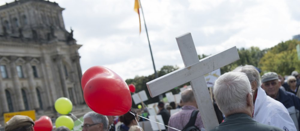 Ein Teilnehmer an der Demonstration "Marsch für das Leben" hält ein weißes Kreuz am 16.09.2017 in Berlin auf der Wiese vor dem Reichstag.