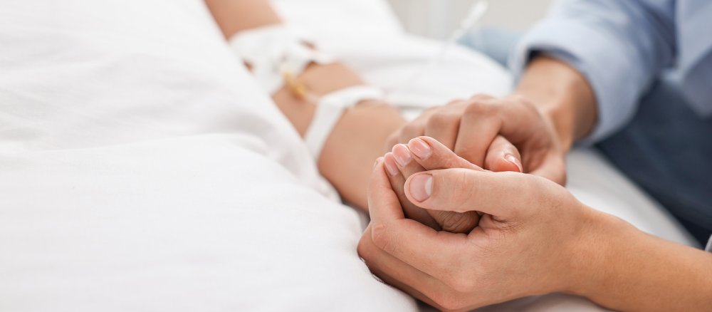 Ein Mann hält die Hand einer Frau in einem Krankenhausbett.