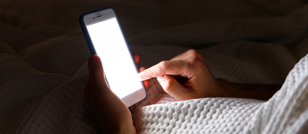 Hände halten ein Handy im Bett
