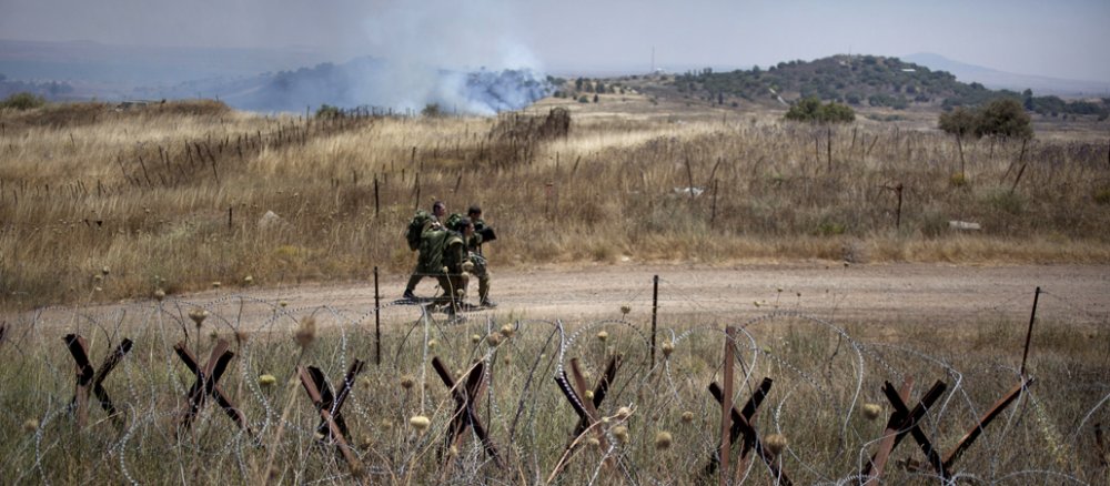 Dicke Panzersperren und Stacheldraht sichern die Grenze zu Syrien. Im Hintergrund gehen drei Soldaten einen Weg entlang.