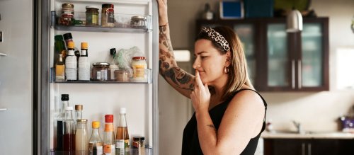 Eine Frau schaut fragend in einen geöffneten Kühlschrank