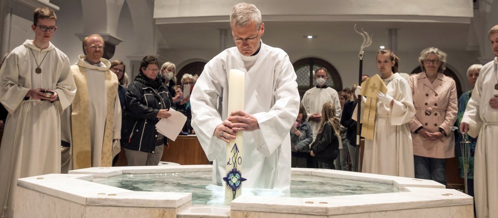 Bischof Wilmer steht mit der Osterkerze in einem Taufbrunnen
