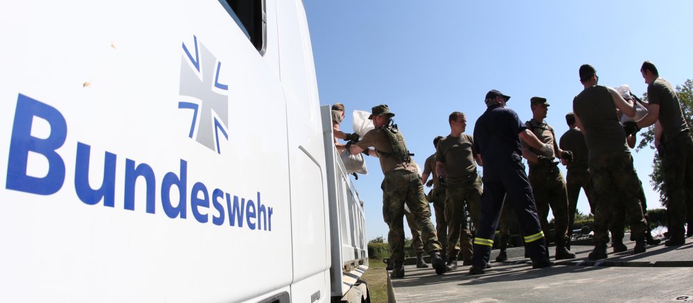 Bundeswehrsoldaten und Helfer beladen über ein Amphibienfahrzeug als Rampe einen LKW der Bundeswehr mit Sandsäcken.