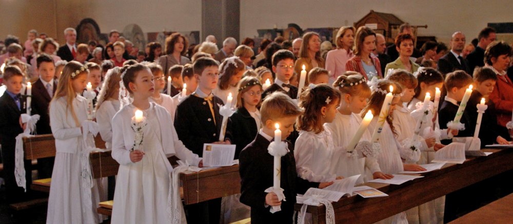 Kommunionkinder stehen mit ihren Kerzen in der Kirchenbank.