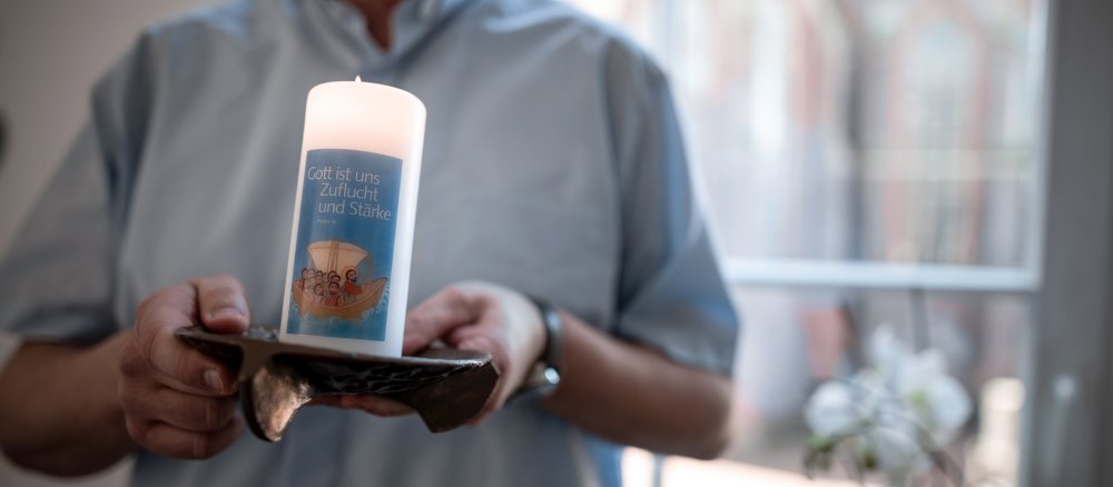 Ein Mann hält eine brennende Kerze und steht vor einem Fenster