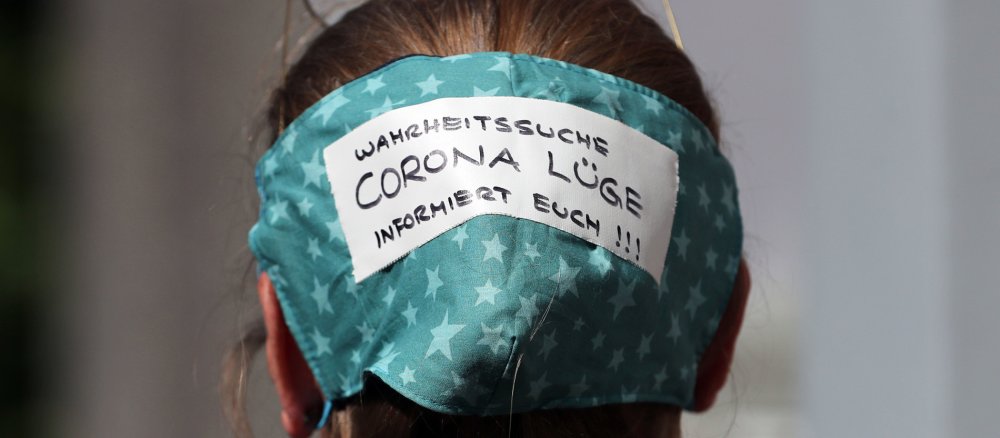 Eine Frau hat ihre Atemschutzmaske auf dem Hinterkopf mit der Aufschrift Corona Lüge