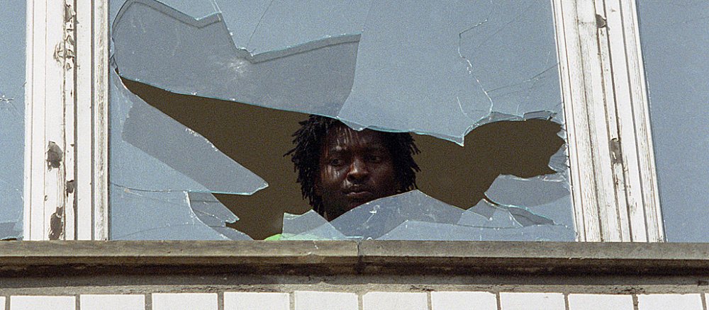 Ein Asylbewerber schaut aus einem bei Krawallen im September 1991 zerbrochenen Fenster in einem Wohnheim für Ausländer im sächsischen Hoyerswerda.